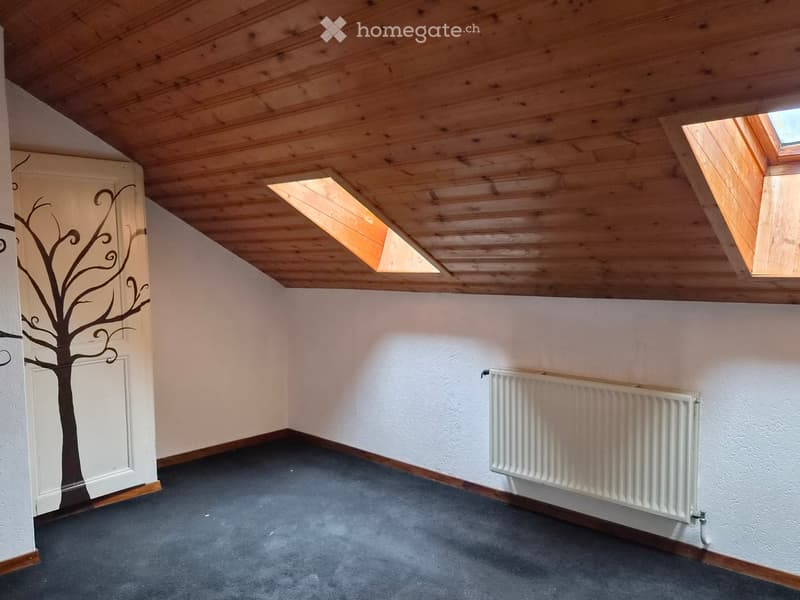 Empty room with wooden slatted ceiling, skylight windows, grey carpet, white walls, and a radiator.