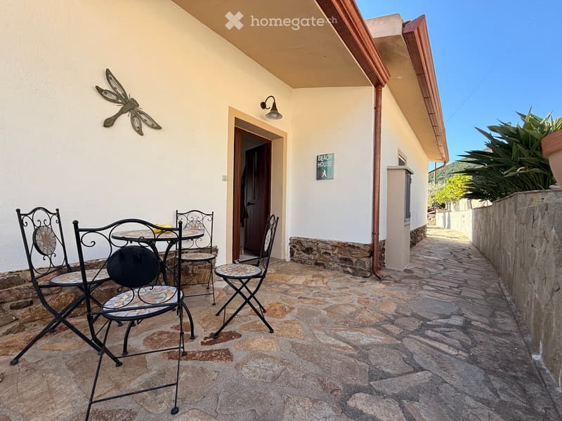 Balcony with stone flooring, metal table and chairs, decorative wall art, and a sign reading "BEACH HOUSE".