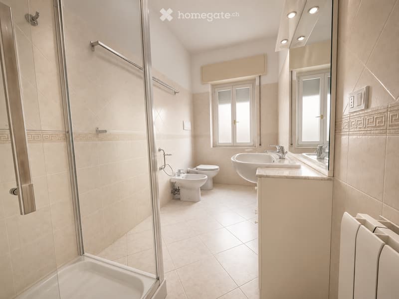 Modern bathroom with beige tiles, a glass-enclosed shower, a bathtub, a toilet, a bidet, and a double sink with a large mirror above it.