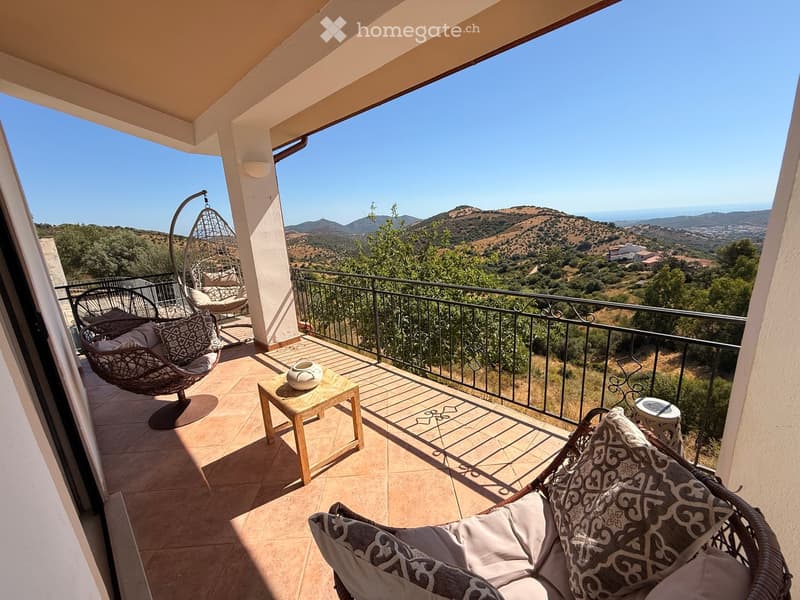 Balcony with wicker chairs, small table, and scenic mountain view.