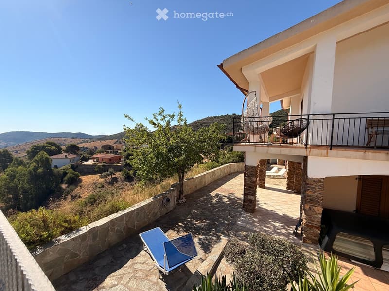 Outdoor patio area with stone flooring, lounge chairs, and a view of the surrounding hills and countryside.