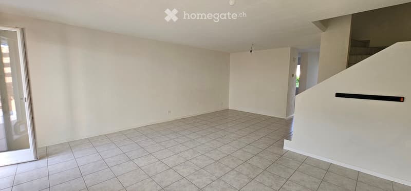 Empty room with tiled floor and white walls, featuring a large glass door leading outside and a staircase in the background.
