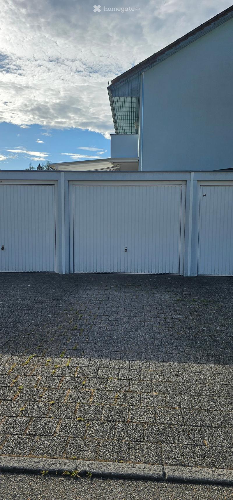 A modern building with a flat roof, white garage doors, and a sleek design, featuring a paved roof area with gravel and small patches of grass.