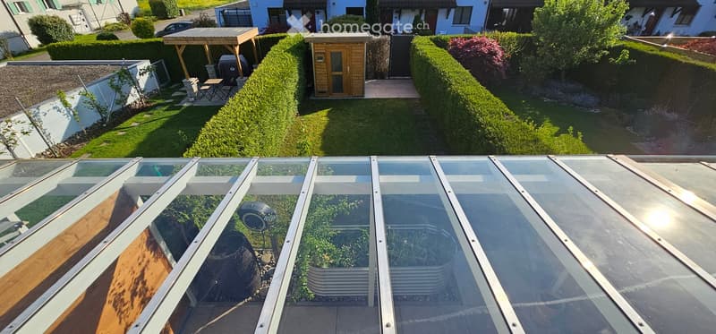 Well-maintained garden with neatly trimmed hedges, a wooden shed, patio furniture, and a greenhouse with glass panels.