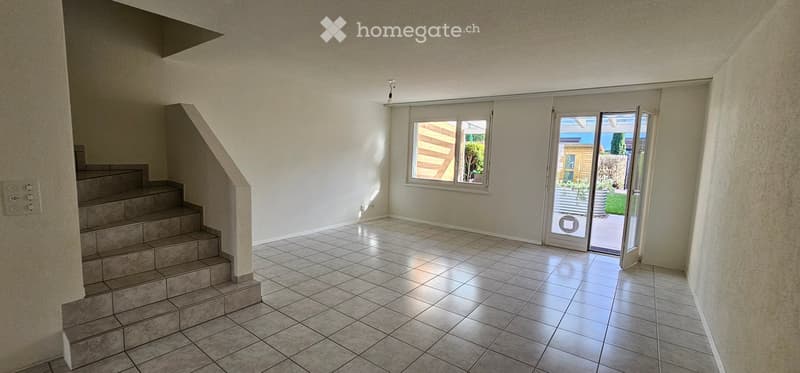 Empty room with tiled floor, staircase leading up, large window, and sliding glass door opening to outdoor area.