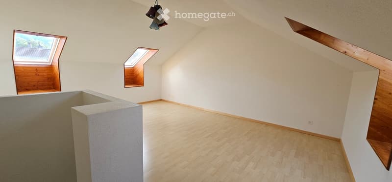Empty attic room with wooden flooring, white walls, skylight windows, and a hanging light fixture.