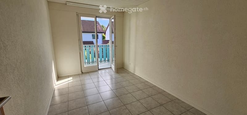 Empty room with tiled floor, white walls, and a sliding glass door leading to a balcony or outdoor area.