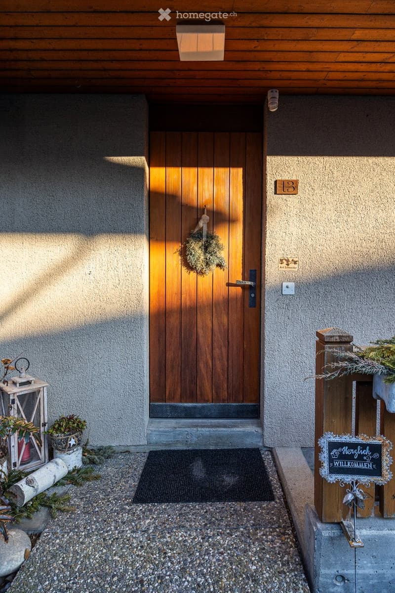 wooden door, concrete wall, welcome sign, small plants, gravel path