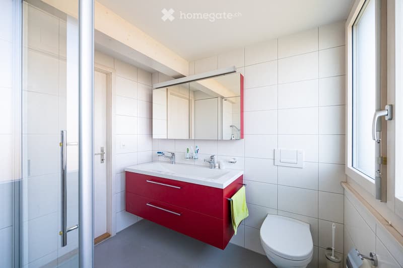 Bathroom with white tiles, red vanity, white sink, mirror, shower, toilet, and window