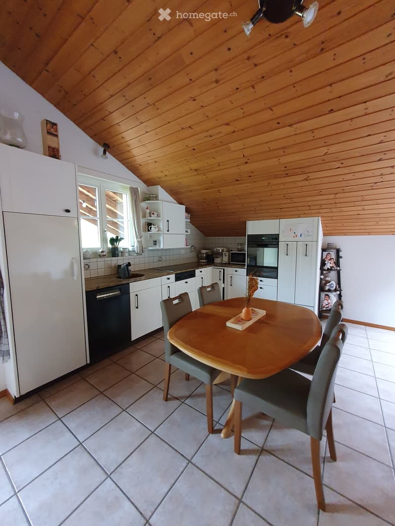 Bright kitchen with white cabinets, wooden ceiling, tiled floor, and a round wooden dining table with four chairs.