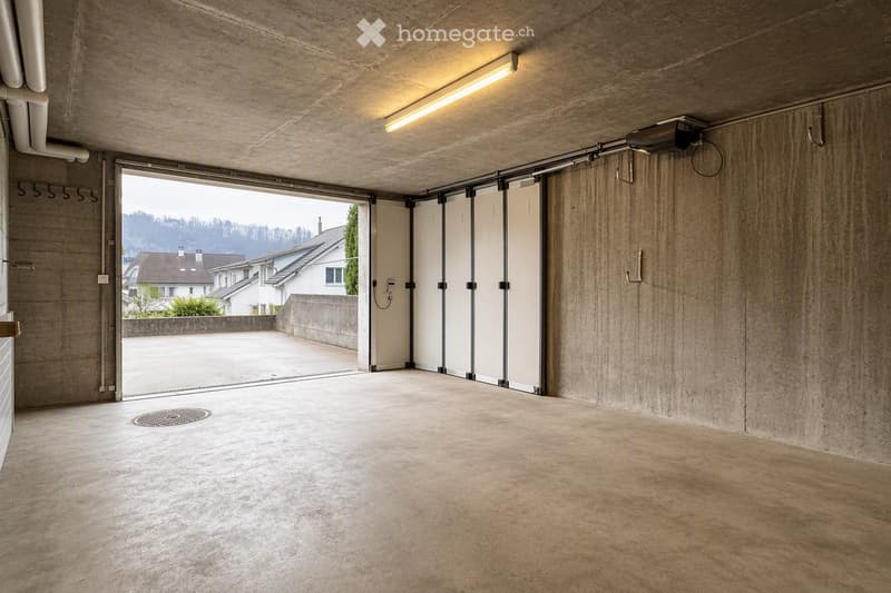 Empty garage with concrete walls and floor, large sliding doors, and a view of the outside area.