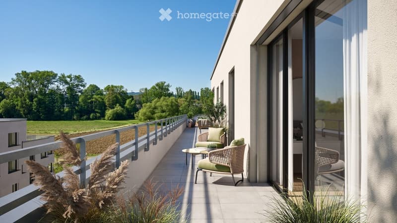 Balcony with modern furniture, including a wicker chair and small table, overlooking a green landscape.