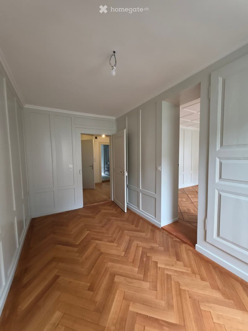 Empty hallway with herringbone wooden flooring, light grey walls, and several doors leading to other rooms.