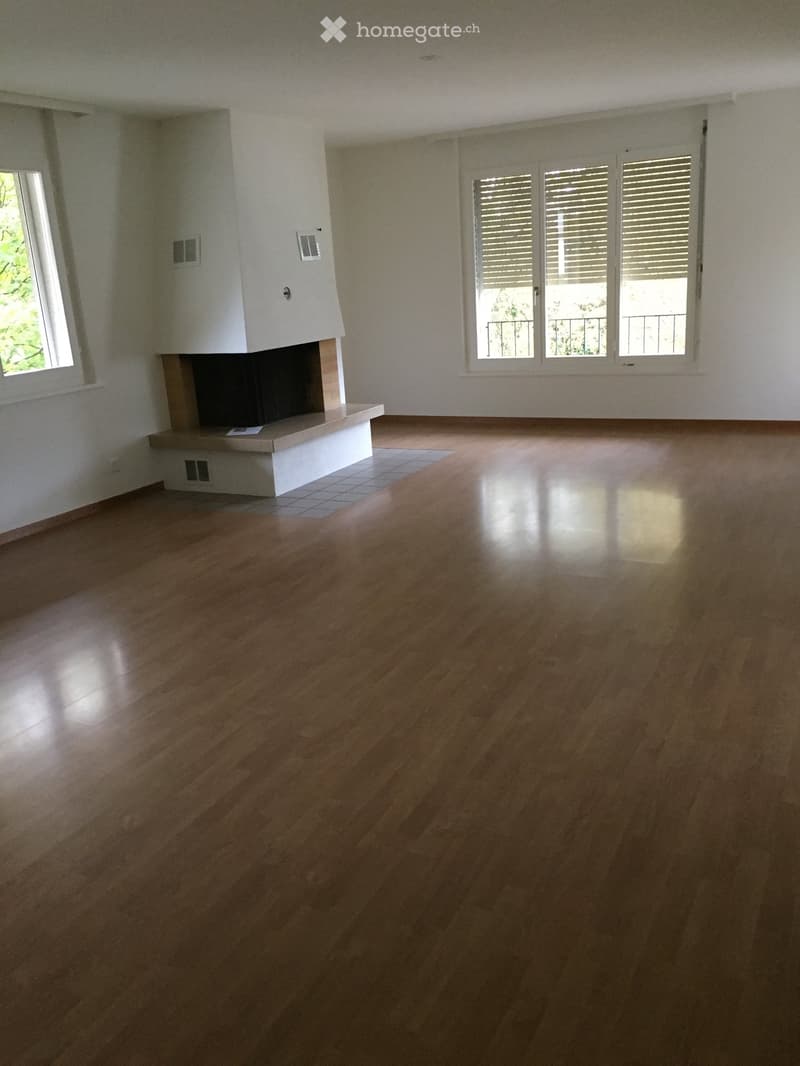 Empty room with wooden flooring, white walls, and a fireplace with a white mantel. Three windows with shutters and a small balcony are visible.