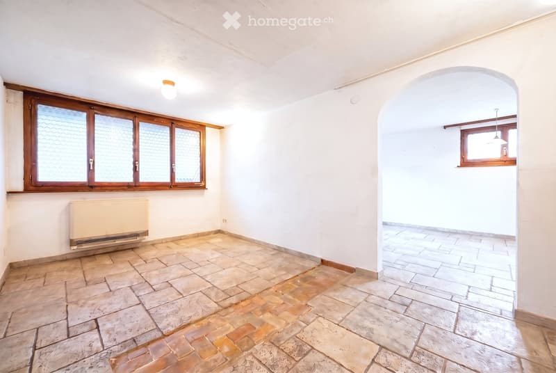 Empty room with tiled floor, white walls, large windows, radiator, and arched doorway leading to another room.