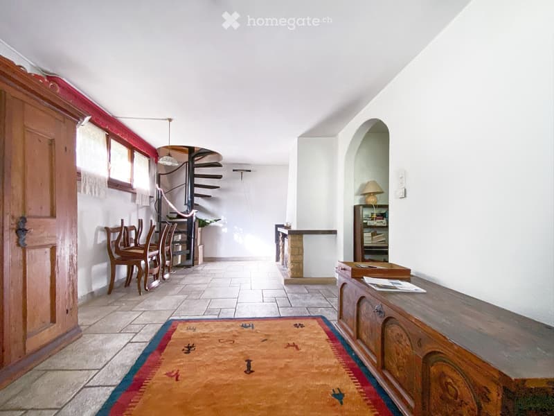 a corridor with stone flooring, a wooden door, a rug, a dining set with chairs, a spiral staircase, and a fireplace