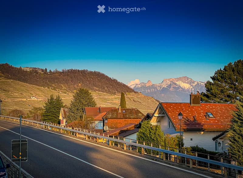 Road leading through the village with a backdrop of mountains, residential houses, and a clear blue sky.