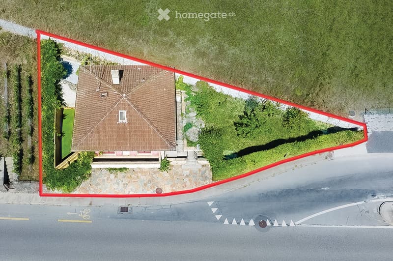 Aerial view of a single-story house with a brown tiled roof, surrounded by a well-maintained garden and a stone pathway leading to the entrance.