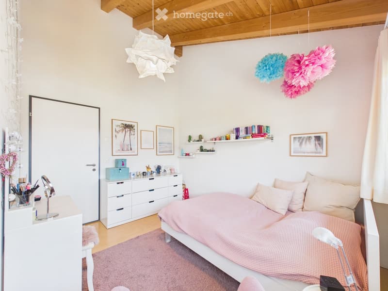 Cozy bedroom with a white bed, pink bedding, a white dresser, shelves, and decorative items.