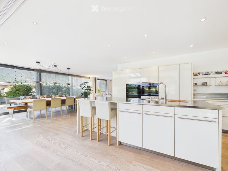 Modern kitchen with white cabinets, a central island, bar stools, a dining area with a table and chairs, and pendant lighting.