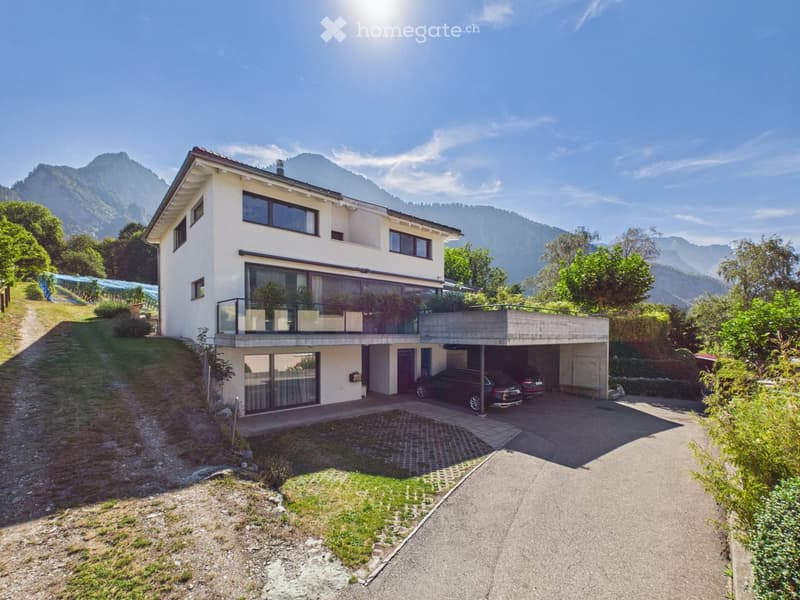 Two-story modern house with white exterior, large windows, balcony, garage, and scenic mountain view.