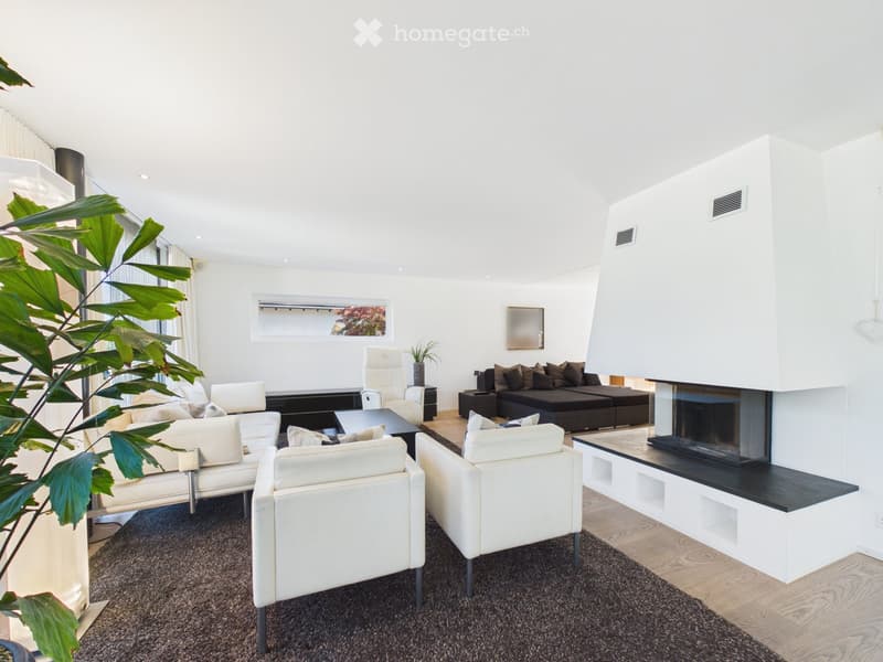 Modern living room with white walls, dark carpet, white leather sofa, armchairs, coffee table, fireplace, and large windows.