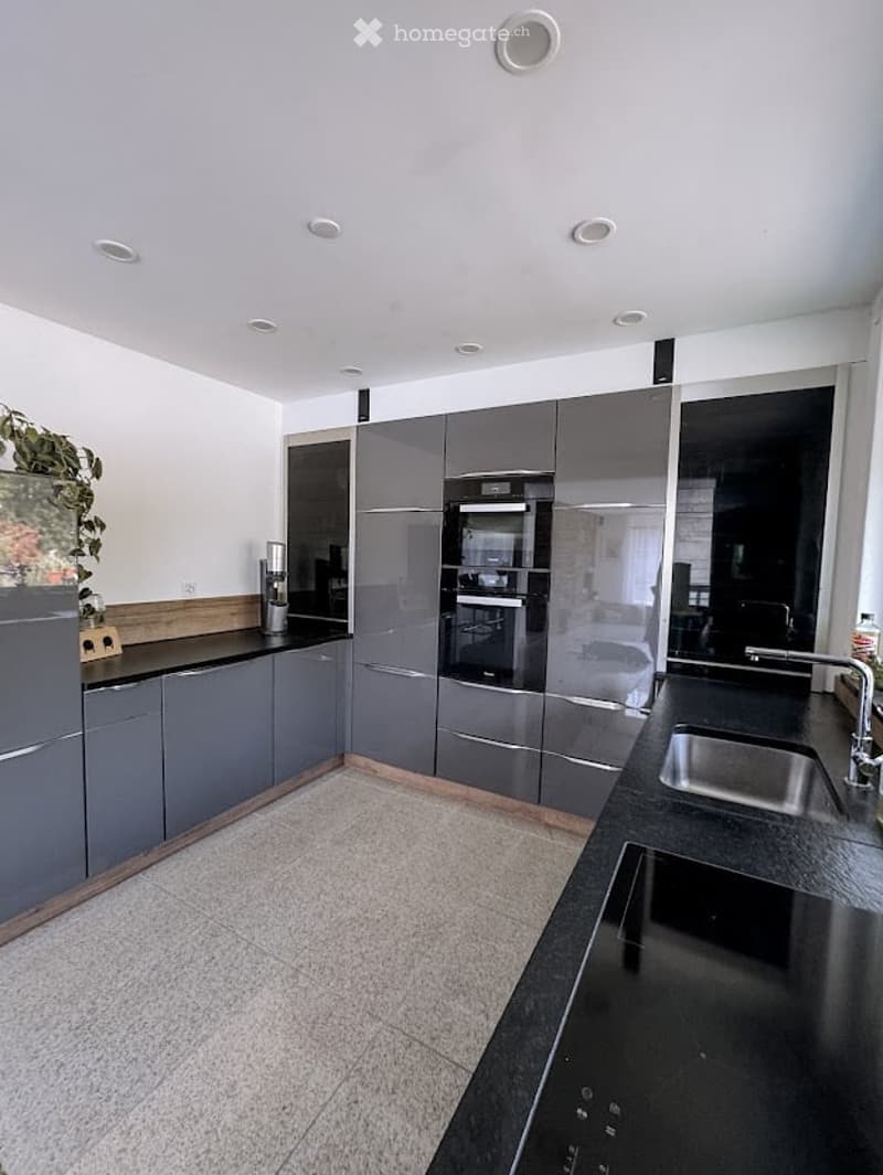 Modern kitchen with grey cabinets, black countertops, stainless steel appliances, and a tiled floor.