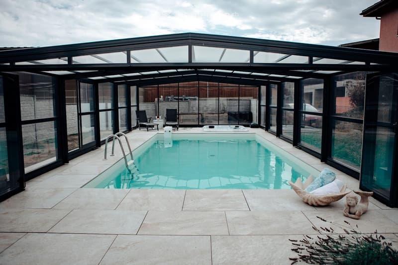Enclosed patio with a swimming pool, lounge chairs, a small table, a hot tub, and decorative statues.