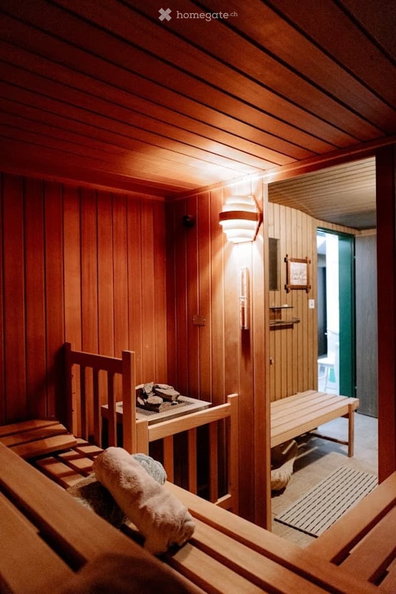 Wooden sauna room with benches, a small table with a fireplace, and a towel on the bench.