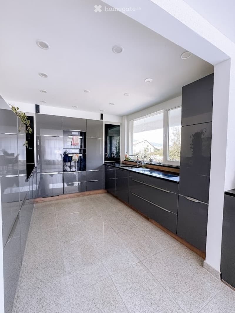 Modern kitchen with grey cabinets, white tiled floor, and large windows offering a view of the outdoors.