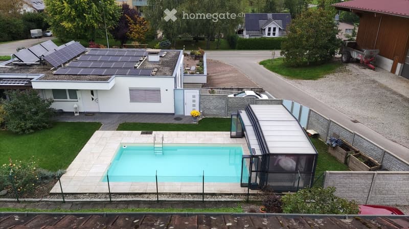 Modern house with a swimming pool in the backyard, surrounded by a fence, with solar panels on the roof and a covered patio area.