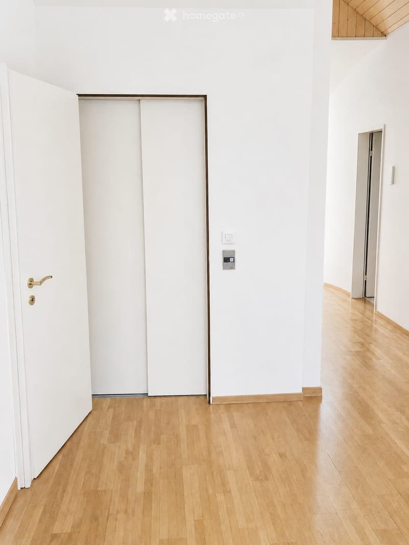 Empty hallway with light wooden flooring, white walls, and a closed sliding door on the left side.