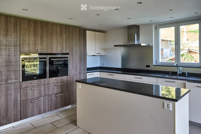 Modern kitchen with dark countertops, light-colored cabinets, stainless steel appliances, and a central island.