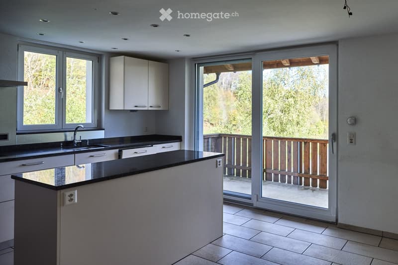 Modern kitchen with white cabinets, black countertops, and a central island. Large windows and sliding glass doors open to a wooden balcony.