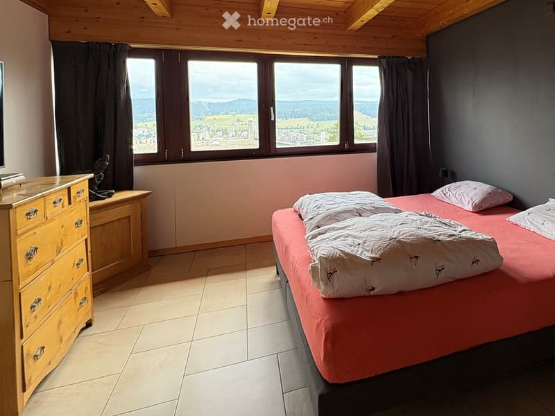 Bedroom with a double bed, wooden dresser, and large windows offering a scenic view of the countryside.