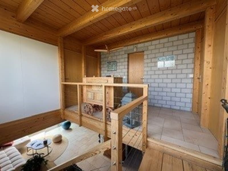 A cozy, wooden-framed living space with a raised platform, a sofa, coffee table, and a small table with chairs. The room features exposed wooden beams and a brick accent wall.