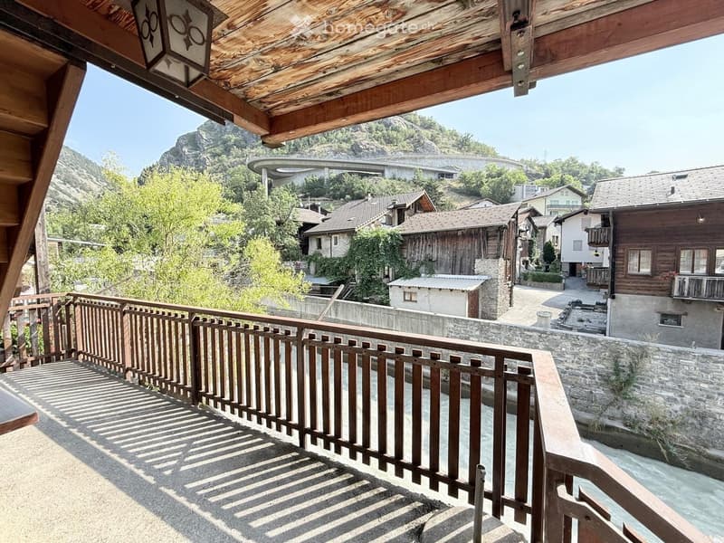 Balcony overlooking a scenic town with traditional wooden houses, a stone wall, and a river below.