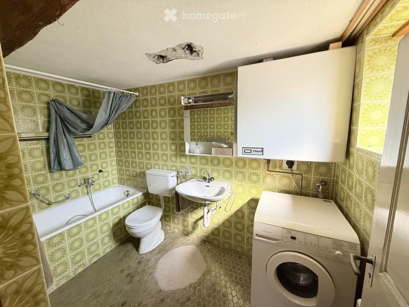 Bathroom with green tiled walls, bathtub, toilet, sink, mirror, washing machine, and a curtain on the shower area.