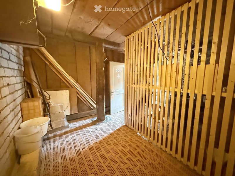 Empty hallway with exposed wooden framing, a staircase leading upwards, and a closed door at the end.