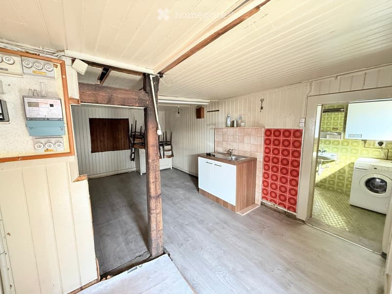 The image shows a partially furnished room with a kitchen area, a sink, a washing machine, and a small dining area with a table and chairs.