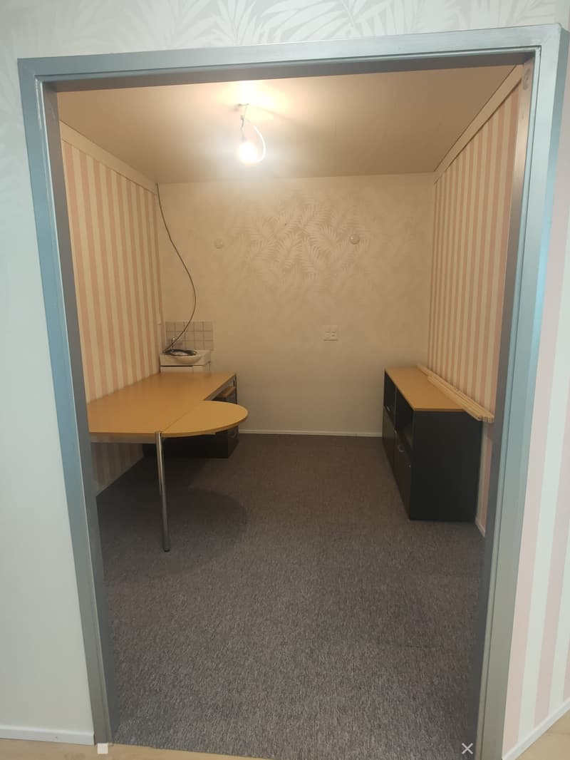 Small furnished room with a desk, cabinet, and carpeted floor.