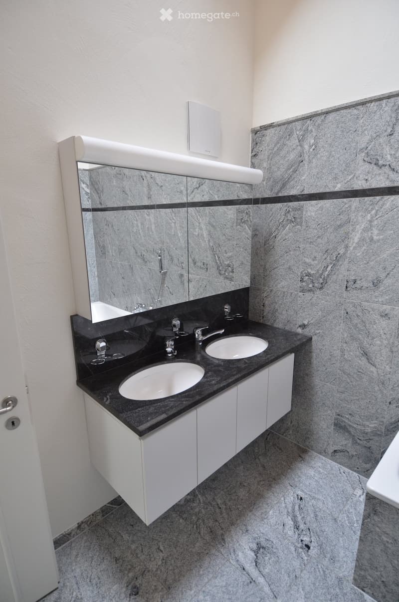Modern bathroom with double sink vanity, black countertop, white cabinets, and large mirror.