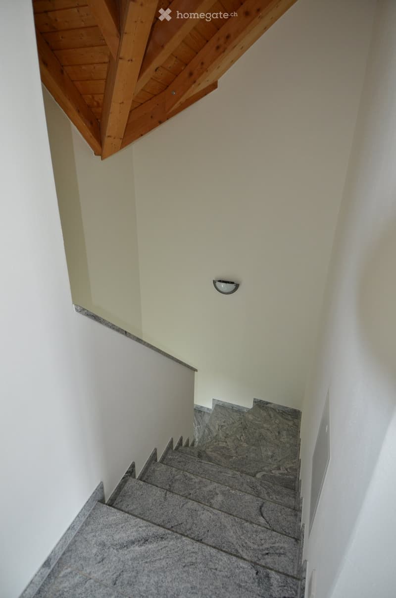 Staircase with marble steps and wooden handrail, light fixture on wall, wooden ceiling beams.