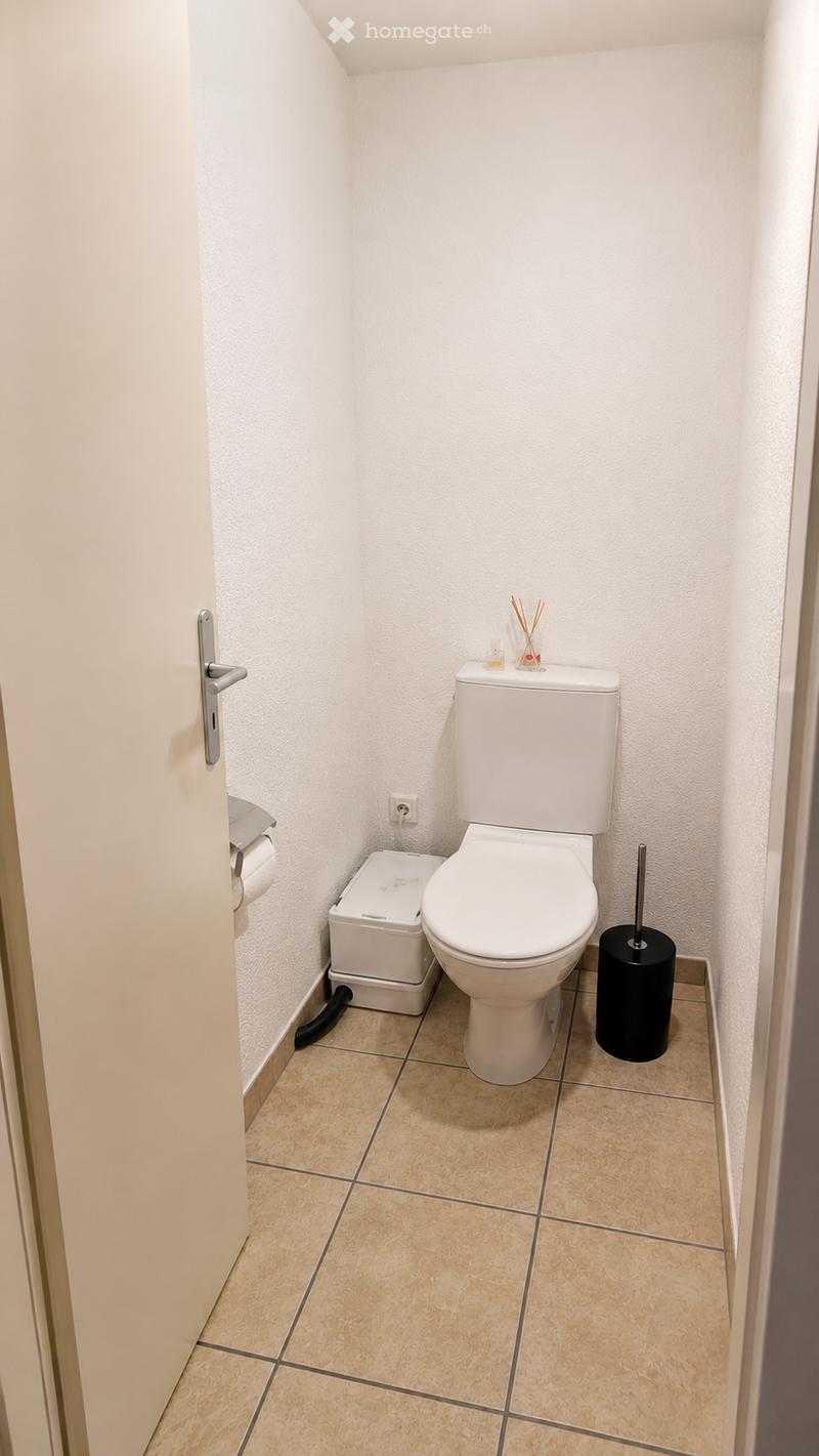 A compact bathroom with a toilet, toilet paper holder, trash bin, toilet brush holder, and a small decorative candlestick on the tank.