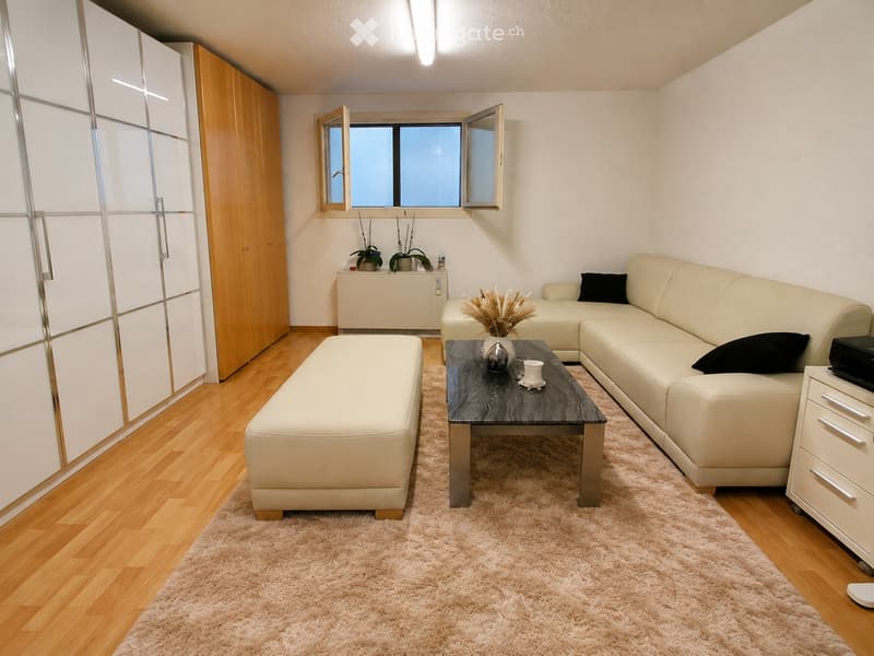 Modern living room with light-colored leather sofa, coffee table, ottoman, side table, and decorative plants.