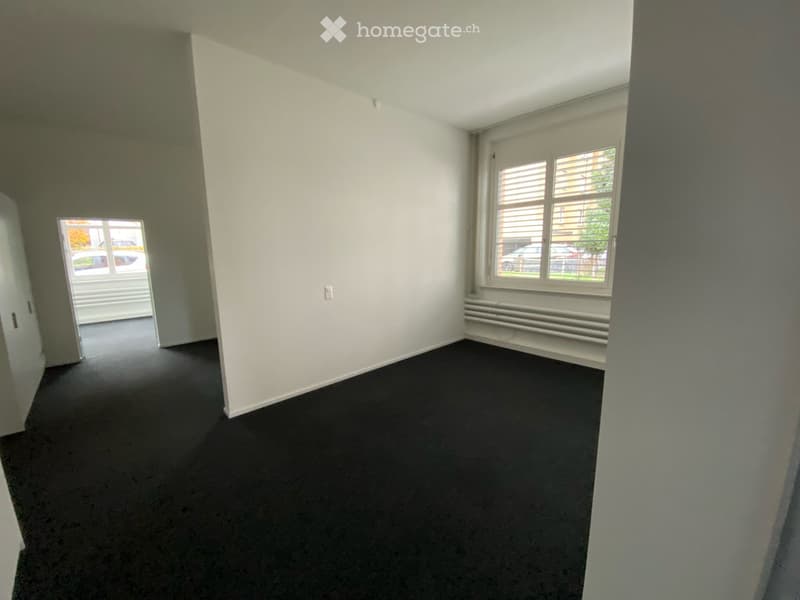 Empty room with white walls, dark carpet, and two windows with blinds. No furniture or equipment visible.