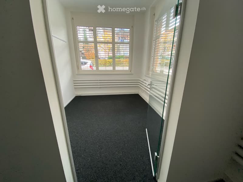 Empty room with grey carpet, white walls, large windows with blinds, and a glass door leading outside.