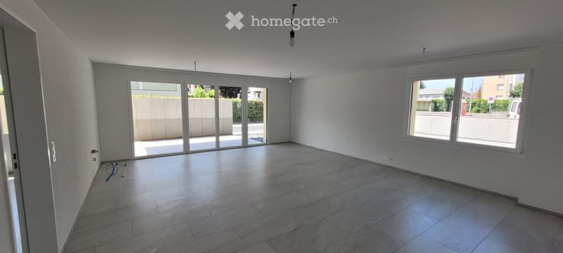 Empty room with tiled floor, large windows, and sliding glass doors leading to an outdoor area.
