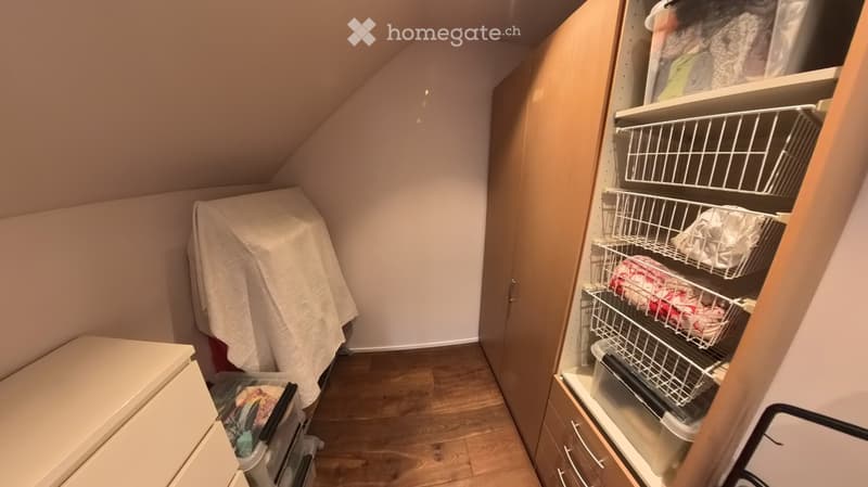An attic storage space with wooden flooring, slanted ceilings, and built-in shelving units containing plastic bins and baskets.