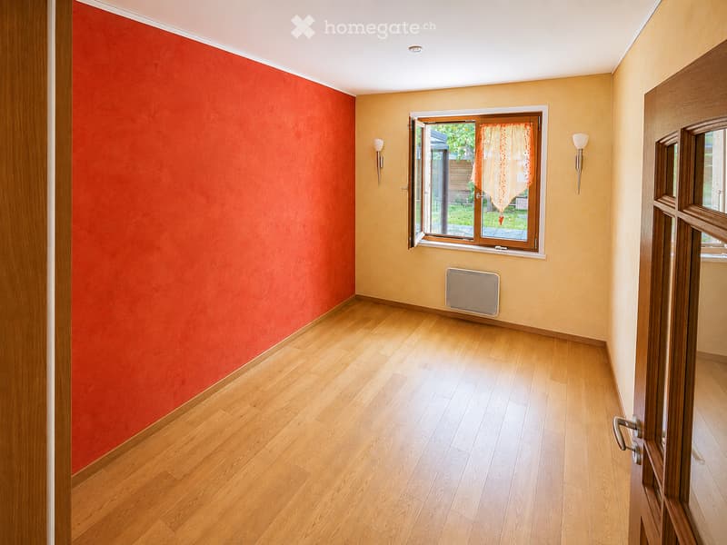 Empty room with wooden flooring, red and yellow walls, a window with a sheer curtain, and a radiator. No furniture or personal items are present.